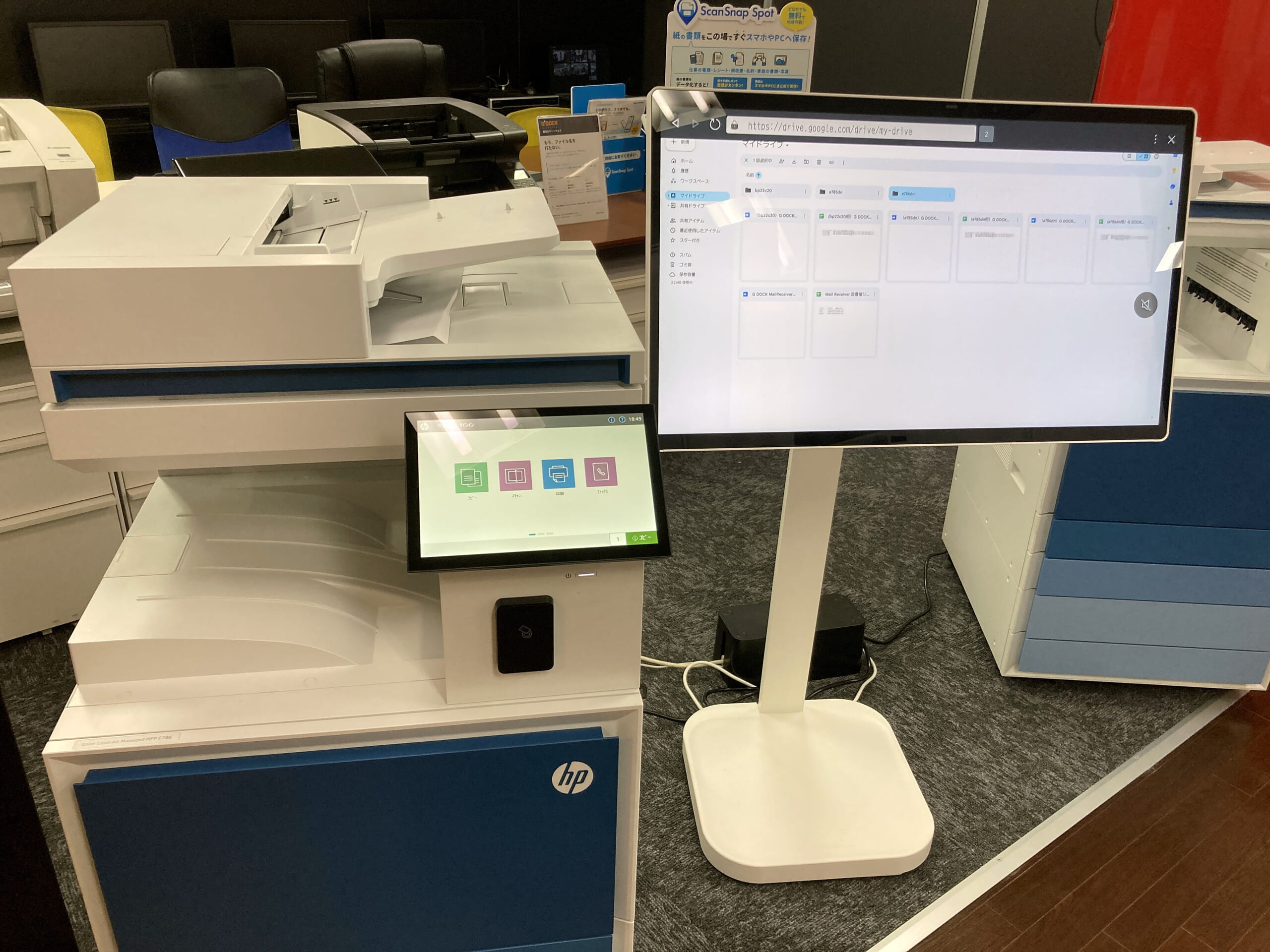 秋葉原ショールームに展示中のHP複合機と、仕分けされた書類フォルダを映すモニター